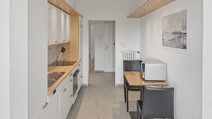 Un pasillo estrecho con una cocina a la izquierda, una zona de comedor con microondas a la derecha y una puerta que da a otra habitación.