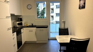 Cozinha compacta com armários brancos, micro-ondas e área de jantar com mesa e cadeiras.