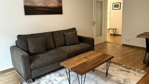 Uma sala de estar com um sofá cinzento, uma mesa de centro de madeira e um quadro na parede.