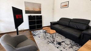 Un salon moderne avec un canapé en cuir noir, un fauteuil gris, une table basse, un meuble TV noir et un tapis à motifs.