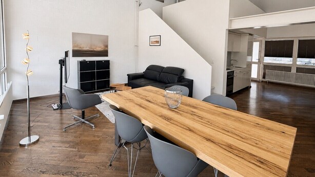 Un intérieur moderne avec une longue table en bois, des chaises grises, un canapé noir et un lampadaire.