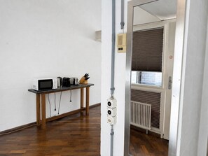 A room with a wooden floor, a white brick wall, a table with a microwave, toaster, and knife block, and a radiator.