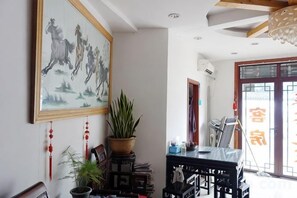 Quarto com pintura tradicional chinesa, planta em vaso e mesa de jantar.