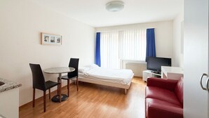 Een hotelkamer met een bed, een klein tafeltje met twee stoelen, een rode bank, een televisie en een raam met gordijnen.