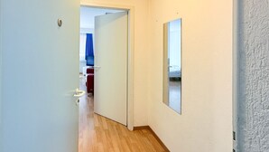 Een smalle gang met een houten vloer, een witte deur links en een spiegel aan de rechter muur.