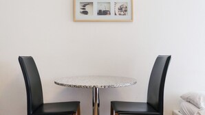 Een kleine ronde tafel met een granieten blad, omringd door twee zwarte stoelen met houten poten. Daarboven hangt een lijst met daarin drie afbeeldingen.