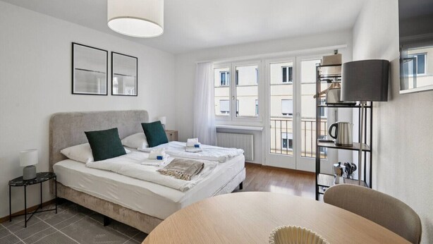 Ein modernes Hotelzimmer mit Bett, Nachttischen, einem runden Tisch und Blick ins Freie.
