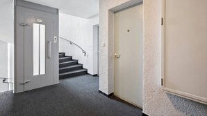 Ein Flur mit Teppichboden, einer Treppe und zwei Türen, über einer davon befindet sich ein Schild.