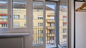 Ein Zimmer mit einer großen Schiebeglastür, die auf einen Balkon führt. Der Balkon ist mit einem Metallgeländer versehen und bietet Blick auf eine Wohngegend mit mehreren Gebäuden.