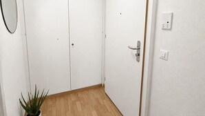A room with a wooden floor, white walls, a door with a handle, a small potted plant, and a wall-mounted light switch.