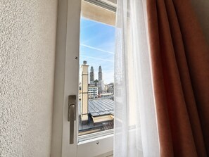 Une fenêtre donnant sur un paysage urbain, avec notamment un immeuble doté de tours.