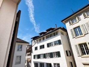 Un immeuble à plusieurs étages, doté d’une façade blanche et de volets verts, et qui présente un balcon à l’étage supérieur.