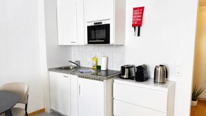 A compact kitchenette with a microwave, sink, and a small countertop with a kettle and coffee maker.