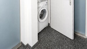 A hotel room with a washing machine and a small storage unit.