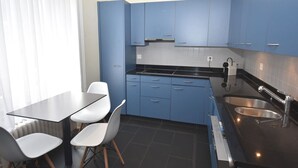 Una cocina compacta con armarios azules, una encimera negra y un lavamanos de acero inoxidable.