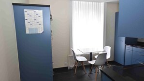 Una cocina compacta con comedor, un refrigerador con calendario y una ventana con persianas.