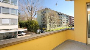 A balcony with a yellow wall, a view of a multi-story building, and a parked car. - Spacious 1BDR near Lake and Opera - Mill 3.11 (Zürich)