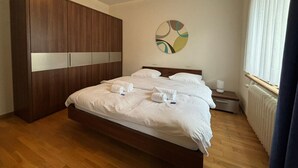 A bedroom with a large bed, a wardrobe, a bedside table, and a wall art piece. - Spacious 1BDR near Lake and Opera - Mill 3.11 (Zürich)