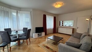 A modern living room with a glass dining table, grey sofas, and a flat-screen TV. - Spacious 1BDR near Lake and Opera - Mill 3.11 (Zürich)