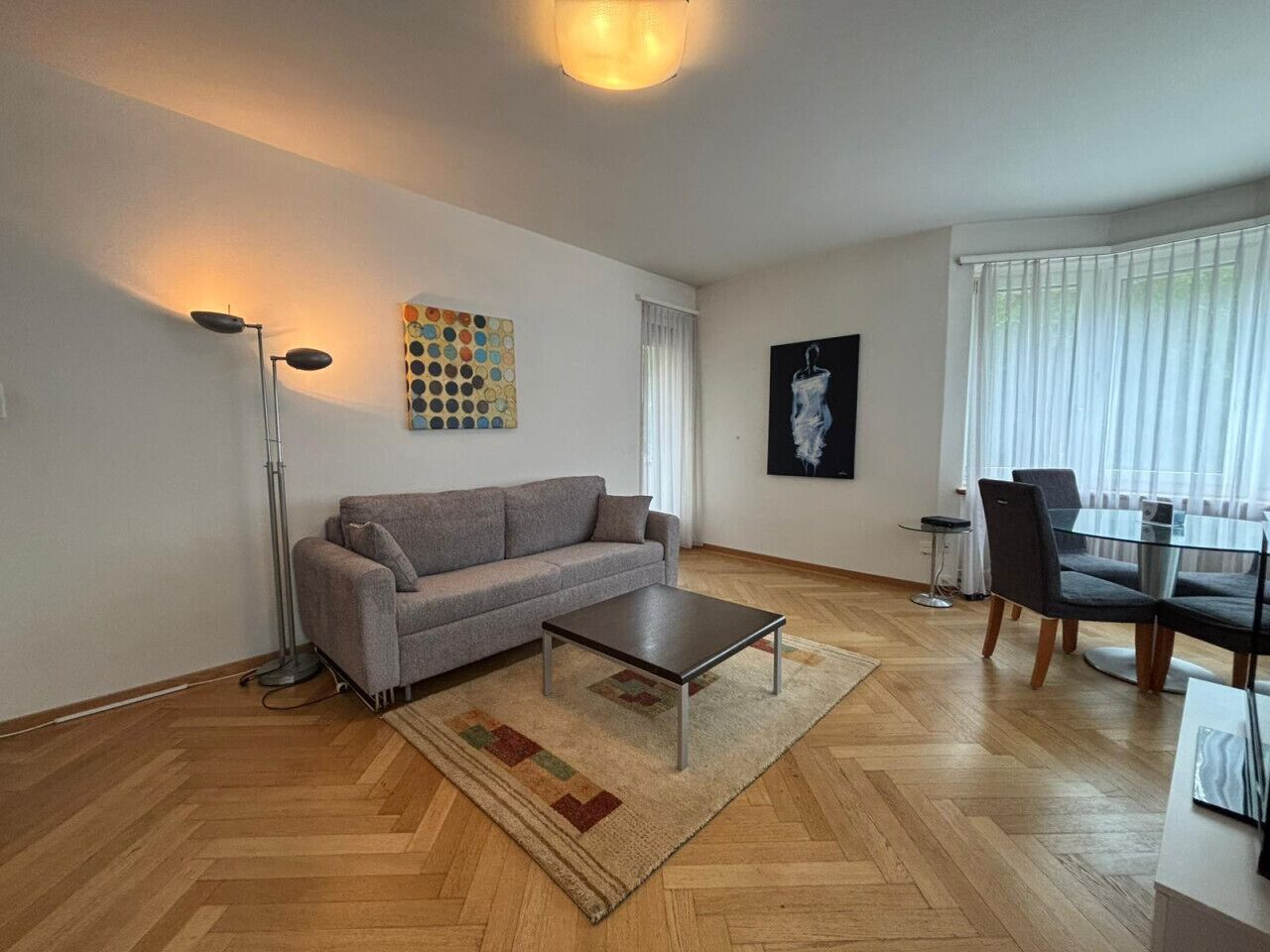 Un salon moderne avec un canapé gris, une table basse, un lampadaire et un coin repas comprenant des chaises et une table.
