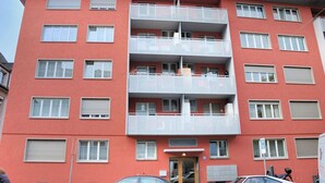 Un edifici d'apartaments de diversos pisos amb balcons, una entrada central i una zona d'aparcament al davant.