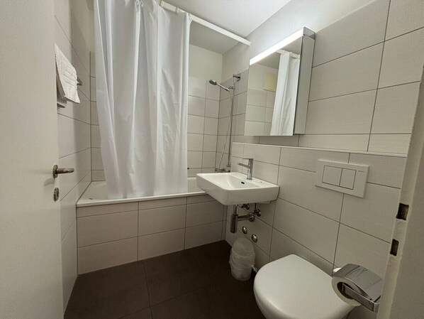 Een kleine, schone badkamer met een badkuip, wastafel en toilet.