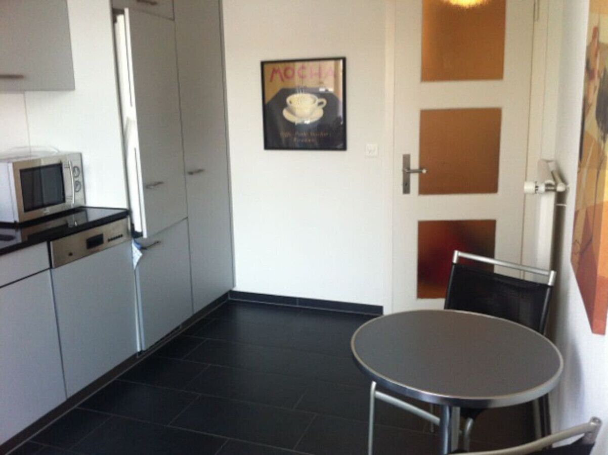 Une cuisine compacte équipée d’un four à micro-ondes, d’une petite table à manger et de chaises. Un tableau représentant une tasse de café est accroché au mur.