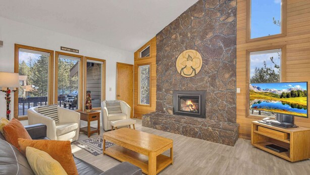 A modern living room with a stone fireplace, large windows, and a television. - Located in heart of Sunriver, complex pool access! (Sunriver)