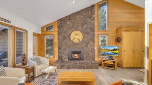 A spacious living room with a stone fireplace, wooden accents, and large windows. - Located in heart of Sunriver, complex pool access! (Sunriver)