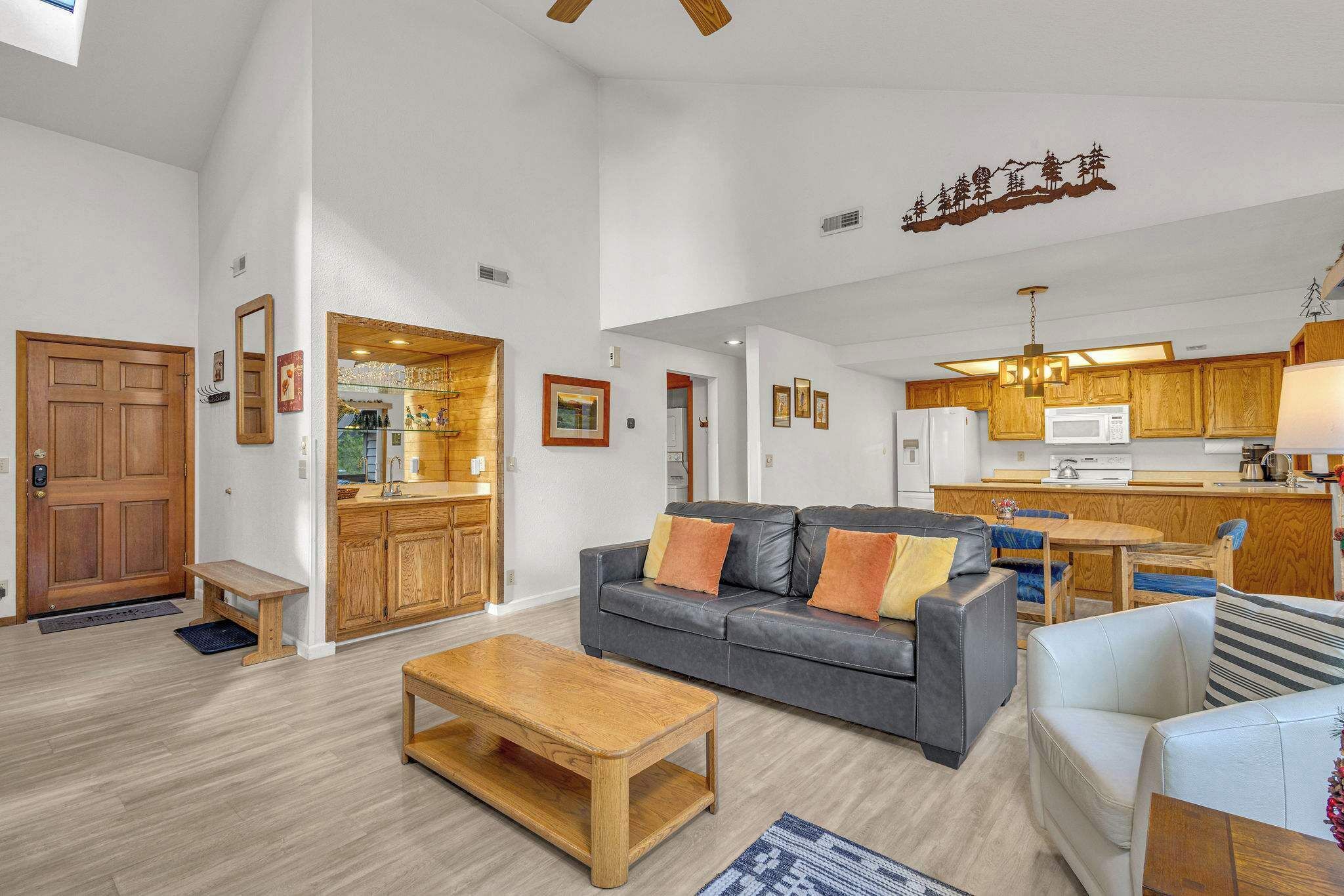 A spacious living area with a grey sofa, wooden coffee table, and a kitchen in the background.