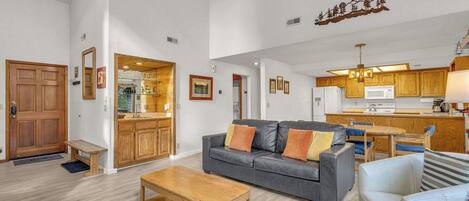 A spacious living area with a grey sofa, wooden coffee table, and a kitchen in the background.