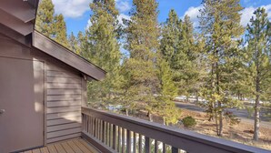 A wooden deck with a railing overlooking a forested area and a road. - Located in heart of Sunriver, complex pool access! (Sunriver)