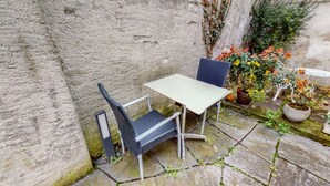 Een stenen muur met een kleine tafel en twee stoelen. Er staan potplanten en bloemen in de buurt.