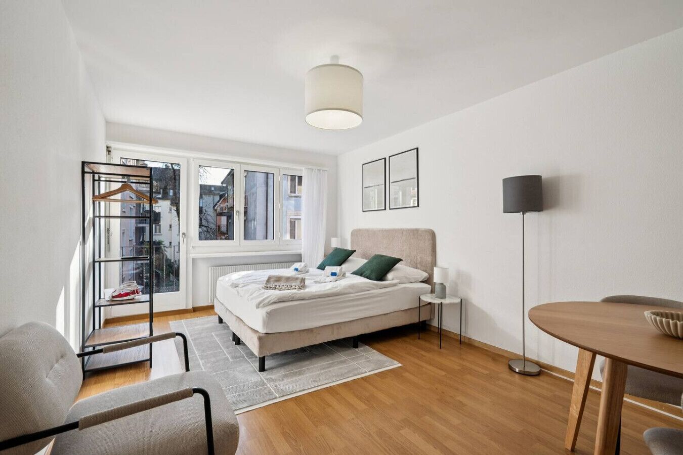 Une chambre à coucher moderne, avec un lit, une table de chevet, une lampe sur pied, une chaise, une petite table et une vue sur la ville par la fenêtre.