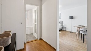 A modern, minimalist room with a wooden floor, a dining area with a table and chairs, and a visible bathroom with a shower. - Studio in the heart of Zurich (Crown 24) (Zürich)