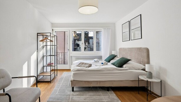 A modern bedroom with a bed, bedside tables, a chair, a window, and a view of the outside. - Studio in the heart of Zurich (Crown 24) (Zürich)