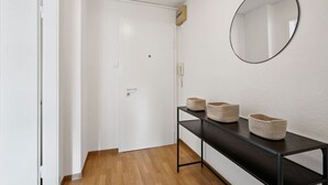 A hallway with a white door, a round mirror, and a black console table with woven baskets. - Studio in the heart of Zurich (Crown 24) (Zürich)