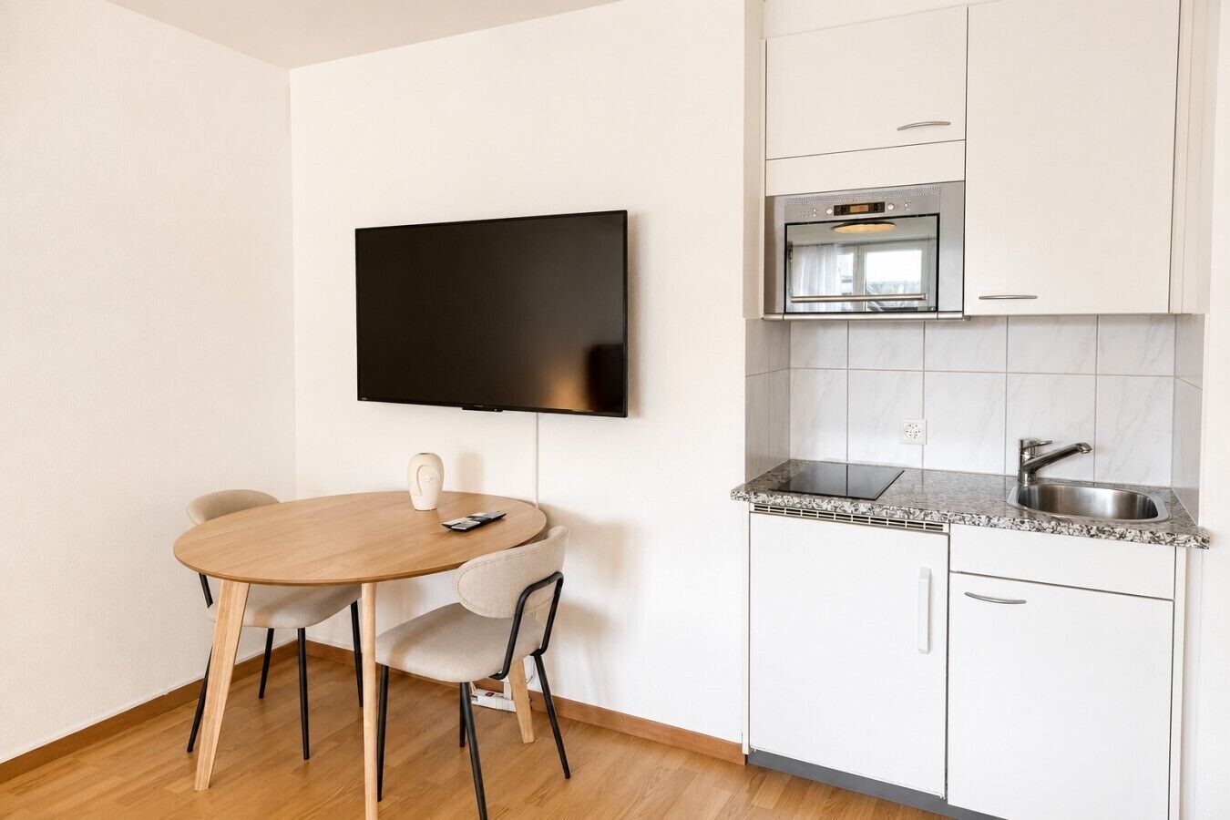 Eine kompakte Küche mit Einbauofen, Spüle und einem an der Wand befestigten Flachbildfernseher.