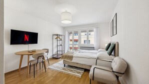 A modern, well-lit room with a bed, a TV mounted on the wall, a small table with chairs, and a coat rack. - City-studio on top floor - Crown 48 (Zürich)