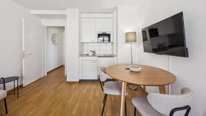 A compact living space with a kitchenette, a dining area with a round table and two chairs, and a flat-screen TV mounted on the wall. - City-studio on top floor - Crown 48 (Zürich)