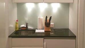 Cozinha compacta com armários brancos, bancada preta e fogão embutido.