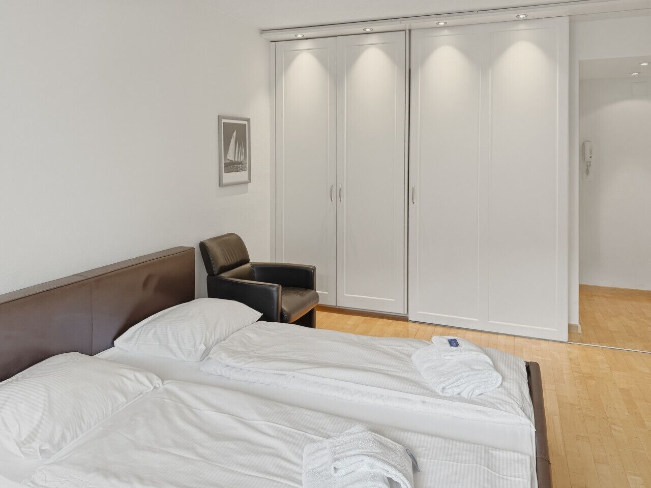 A bedroom with a bed, a chair, a wardrobe, and a framed picture on the wall.