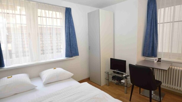 A hotel room with a bed, a desk with a computer, a chair, and a radiator. - Studio at famous location  - Stork 21 (Zürich)