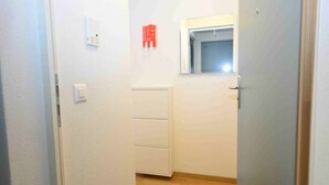 A narrow hallway with a door on the right, a window on the left, and a red emergency exit sign on the wall. - Studio at famous location  - Stork 21 (Zürich)