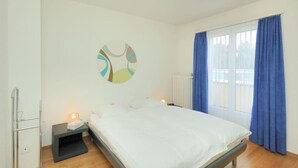 A bedroom with a bed, a bedside table with a lamp, a radiator, and a window with curtains.
