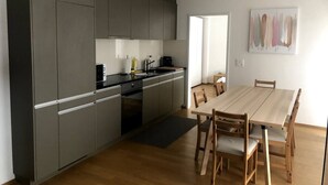 A modern kitchen with grey cabinets, a wooden dining table, and a small dining area.