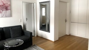 A modern living room with a grey sofa, a glass coffee table, and a large mirror.