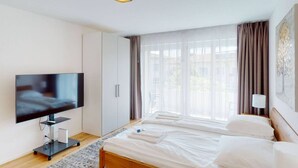 A modern hotel room with a flat-screen TV, a bed, a bedside table, and a window with curtains. - Amazing big studio city center (Sun 7) (Zürich)
