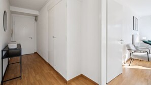 Ein geräumiges Zimmer mit Holzboden, weißen Wänden und einem großen Kleiderschrank. Ein kleiner Tisch mit einem Korb und ein Stuhl in der Ecke sind ebenfalls vorhanden.