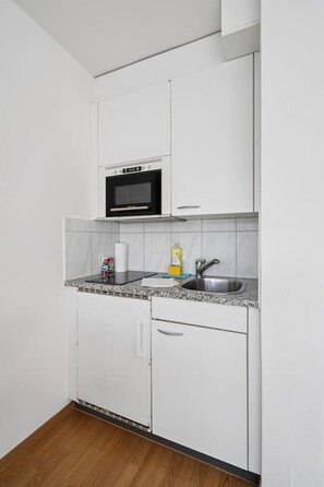 Una cocina compacta con alacenas blancas, microondas, pileta y mesada.